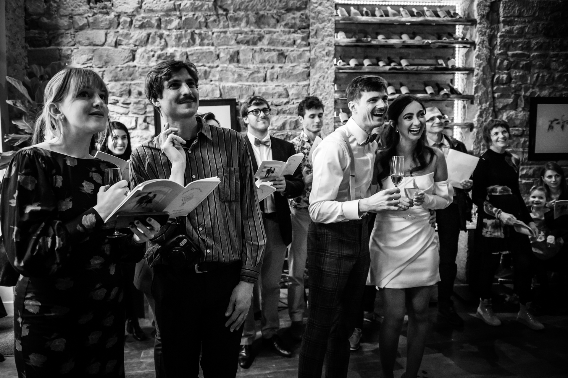 Guests share laughter and tears during bilingual toasts, leaning in with glasses raised at cocktail.